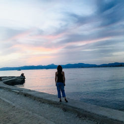 Rear view of man standing on beach against sky during sunset