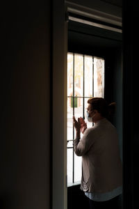 Rear view of woman holding glass window at home