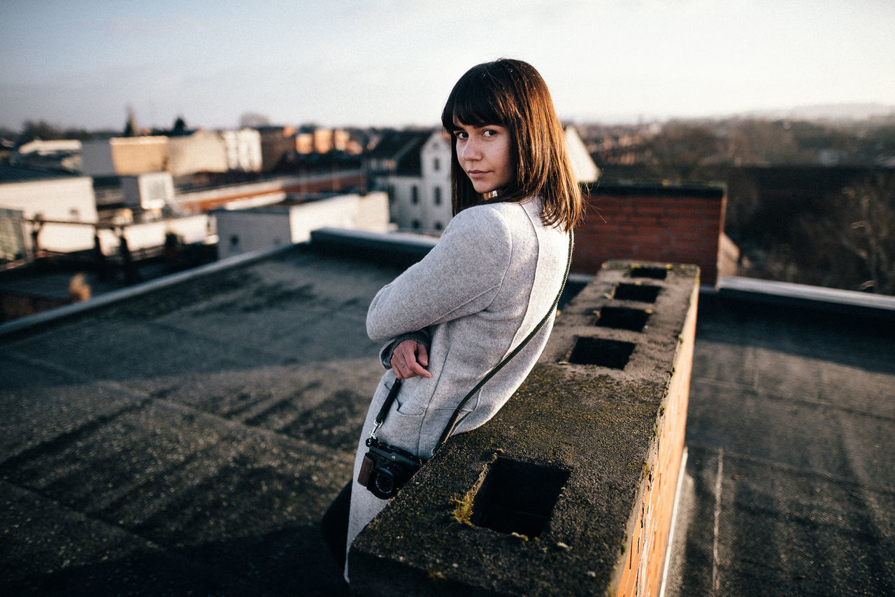 one person, young adult, young women, real people, architecture, looking at camera, building exterior, built structure, portrait, lifestyles, leisure activity, casual clothing, women, hair, day, focus on foreground, city, beautiful woman, hairstyle, outdoors, contemplation, warm clothing