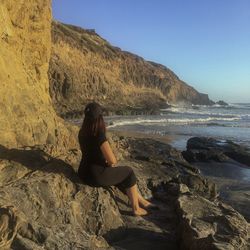 Side view of woman looking at sea while sitting on rock