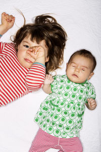High angle portrait of girl rubbing eyes while lying by baby sleeping on bed