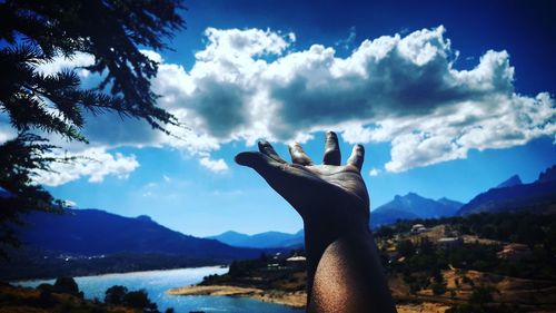 Close-up of woman hand by sea against sky