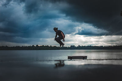 Man jumping over lake against cloudy sky