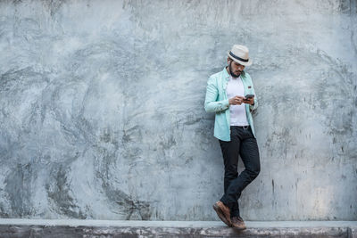 Man using phone while standing against gray wall