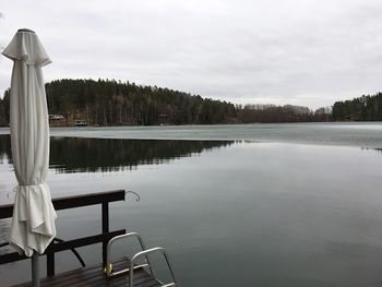 Empty chairs and table by lake against sky