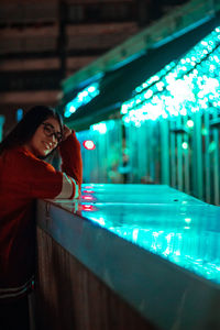 Woman standing by illuminated light at night