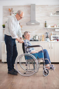 Man pushing disabled woman sitting on wheelchair at home