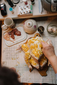 Top view of crop hand of female seasoning uncooked chicken with orange zest while preparing traditional dinner at home kitchen