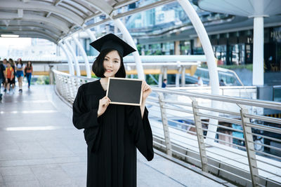 Portrait of woman wearing graduation gown while standing on bridge