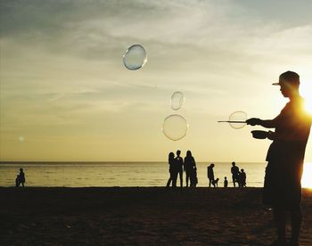 People playing on beach against sky at sunset