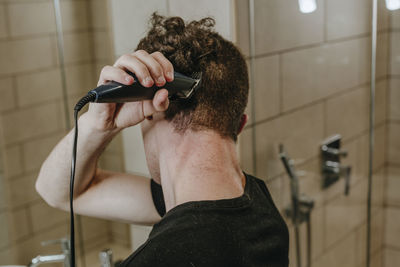 Young man shaving own hair in bathroom at home