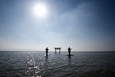 Silhouette people standing on sea against bright sun