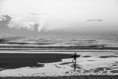 Silhouette man with surfboard walking at beach against sky