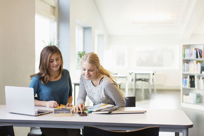 Teenage girls using mobile phone at table in school library