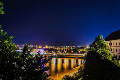 Illuminated buildings by river against sky at night