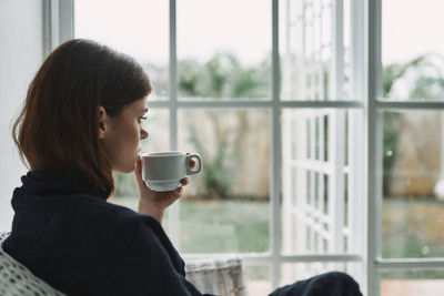 Young woman drinking coffee from window