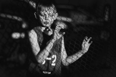 Boy standing with eyes closed seen through chainlink fence