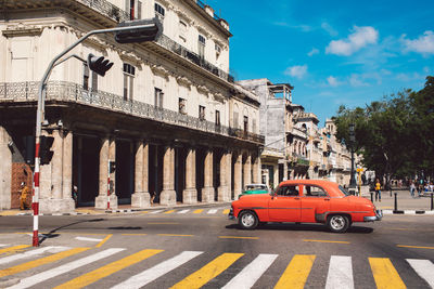 Cars on city street by buildings against sky