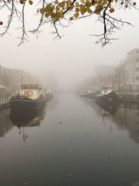 Scenic view of river in city against sky during foggy weather