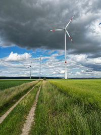 Windmills on field against cloudy sky