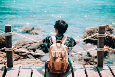 Rear view of man standing by railing against sea