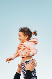 Cropped hands of person catching baby girl against clear sky