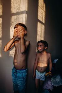 Full length of shirtless boy standing against wall