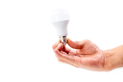 Close-up of hand holding light bulb over white background