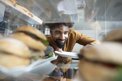 Smiling cafe owner removing burger from display cabinet at coffee shop