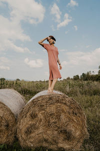 Full length of woman standing on hay bale against sky