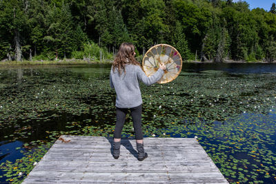 Full length of woman standing by lake against trees