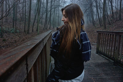 Side view of woman standing by railing on footbridge at forest