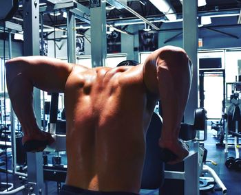 Rear view of shirtless muscular man exercising in gym