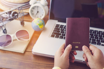 Cropped hands holding passport by laptop on table