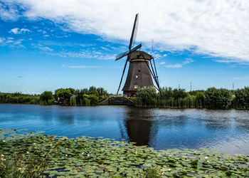 Traditional windmill by lake against sky