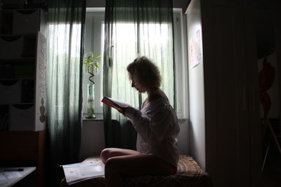 Side view of woman reading book at home