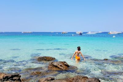 Rear view of woman with arms raised standing in sea