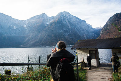 Rear view of friends standing by lake against mountains