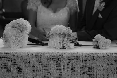 Midsection of bride and bridegroom sitting by flower bouquets on table