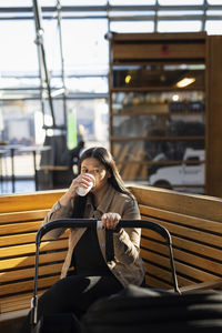 Woman having coffee on bench while looking at pram