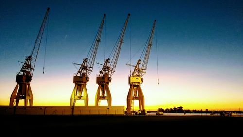 Cranes against sky during sunset