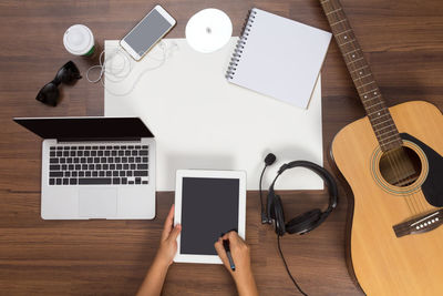 Cropped hands using digital tablet with laptop and guitar on table