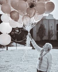 Smiling senior woman holding balloons while standing on land