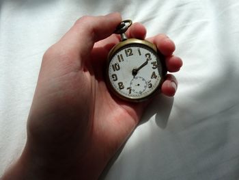 Cropped hand holding old pocket watch on bed