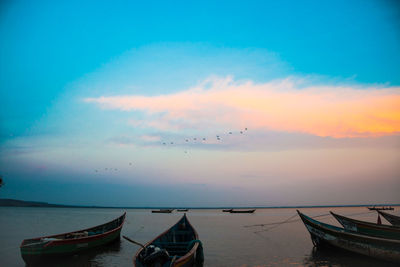 Boats moored in sea against sky during sunset