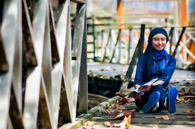 Portrait of young woman standing by railing