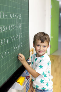 Portrait of boy writing on blackboard in classroom