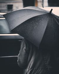 Rear view of person holding wet umbrella during monsoon