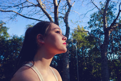 Beautiful woman looking away against trees at park
