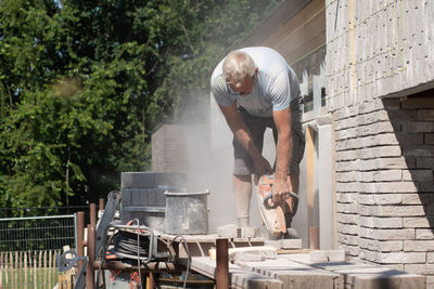 A grayhaired man saw bricks with a concrete saw of the right size for subsequent